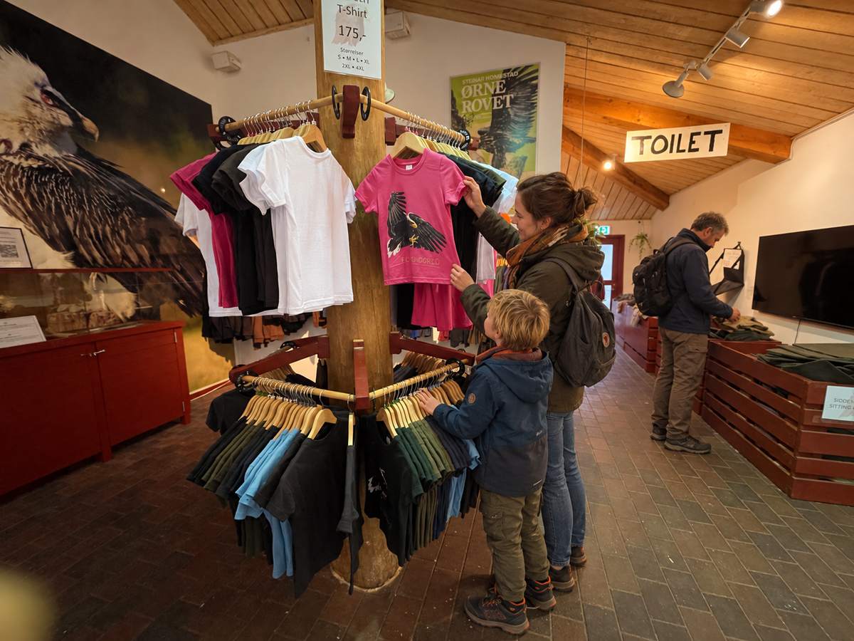En mor og hendes søn kigger på T-shirts med ørnemotiv på et stativ i butikken
