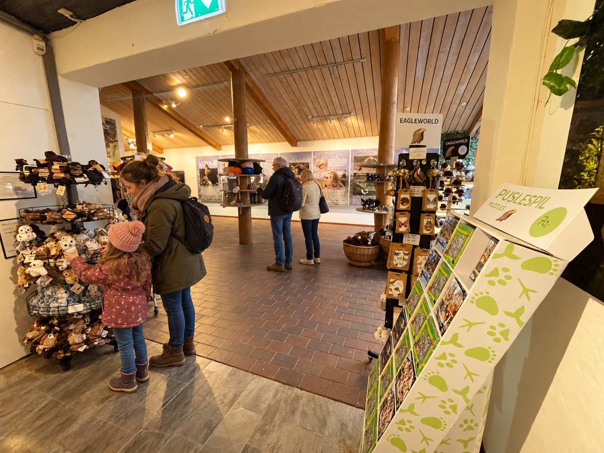 En mor og hendes datter ved de bløde ugler ved indgangen til butikken, ved siden af en stand med puslespil